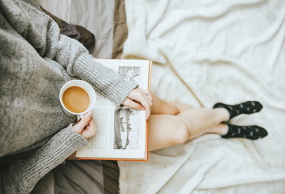 Self-care. A woman sitting down and relaxing with a drink and a book. Photo Credit: Anthony Tran via Unsplash.com